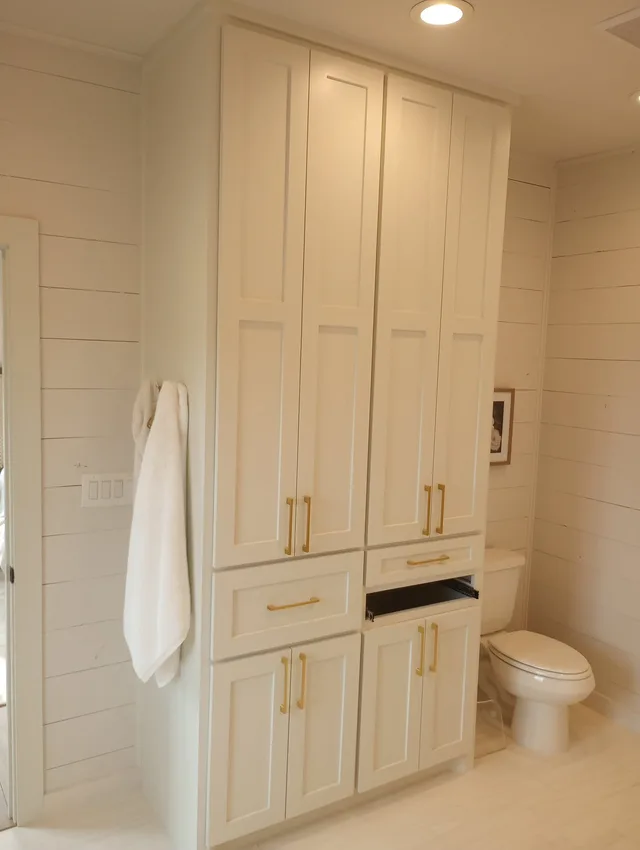 Tall white bathroom linen cabinet tower with gold hardware and shiplap walls
