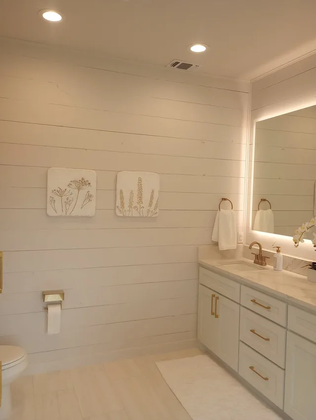 White bathroom vanity cabinets with gold hardware and shiplap accent wall
